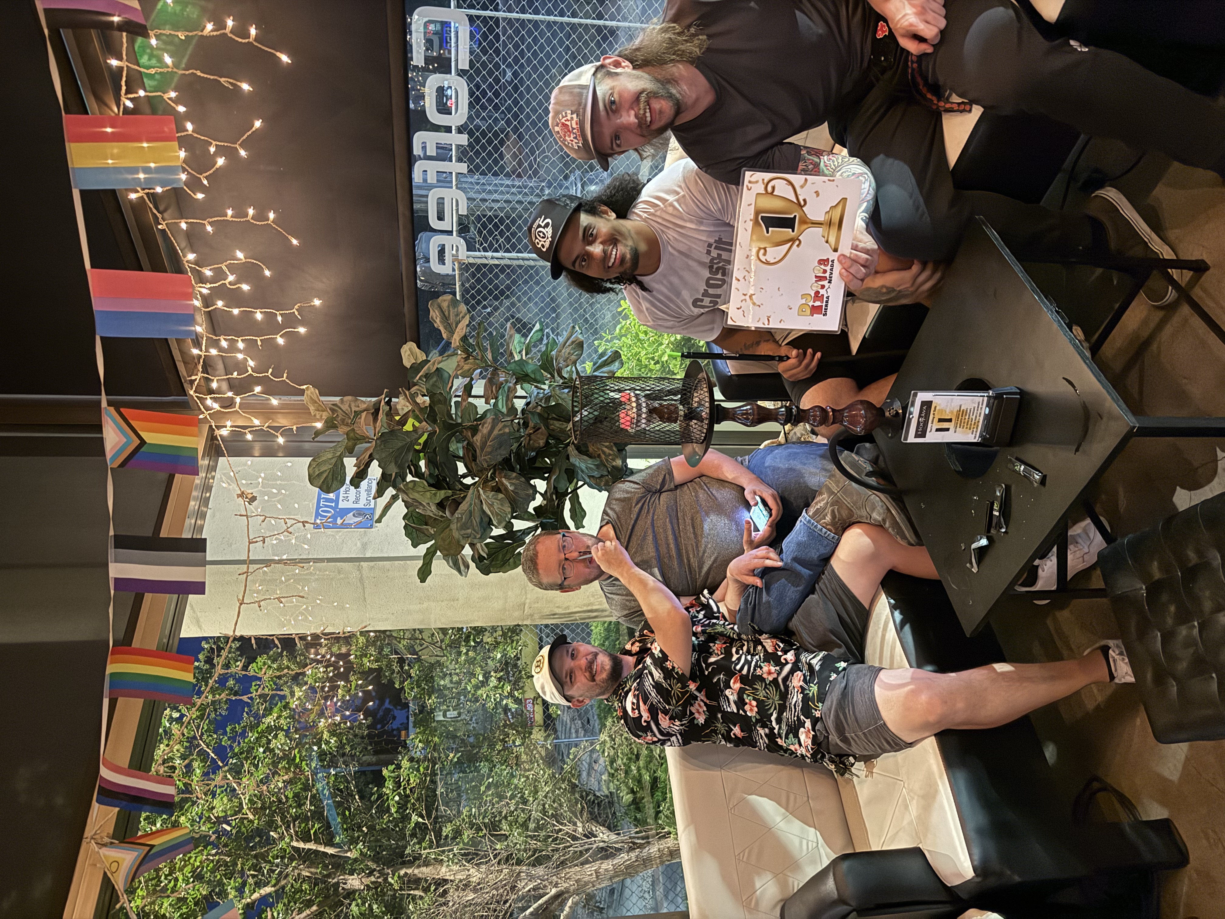 1st place trivia winners holding trophy card at Hookava with pride flags in background