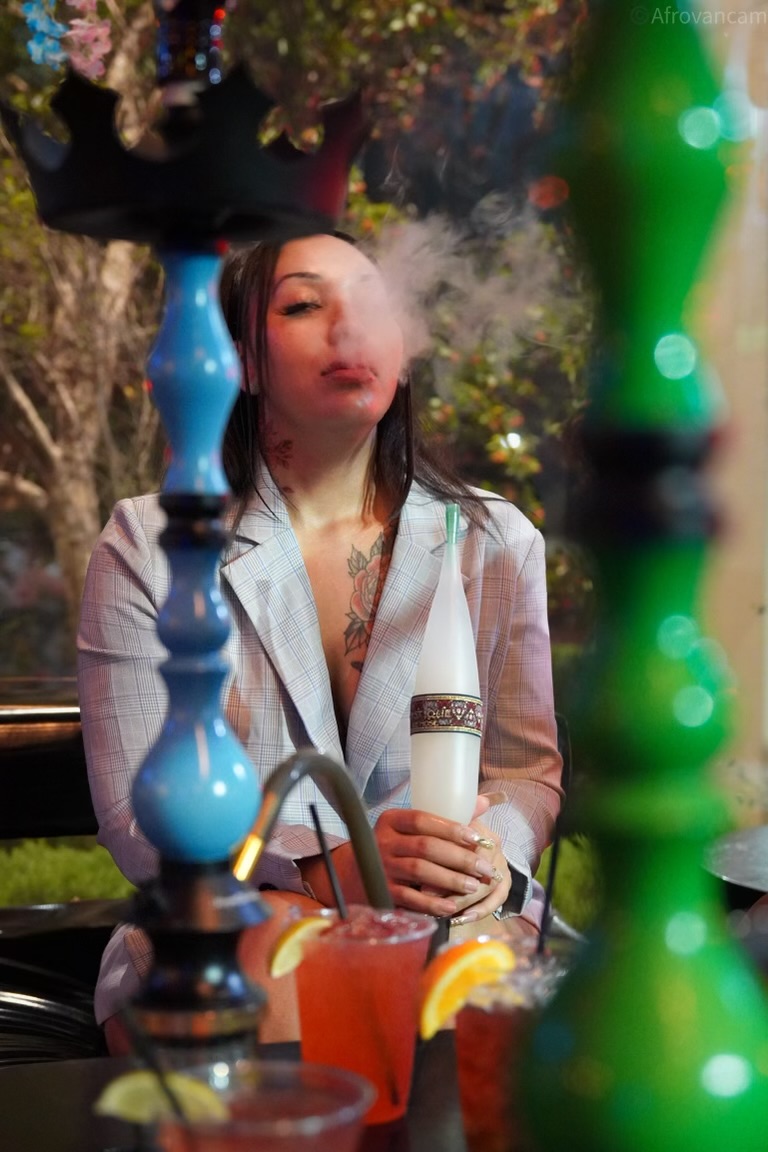 Guest exhaling hookah smoke at Hookava with cocktails and a blue hookah on the table